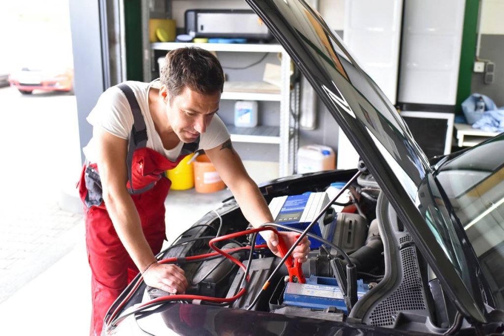 Car mechanic working in repair garage, reloading car battery