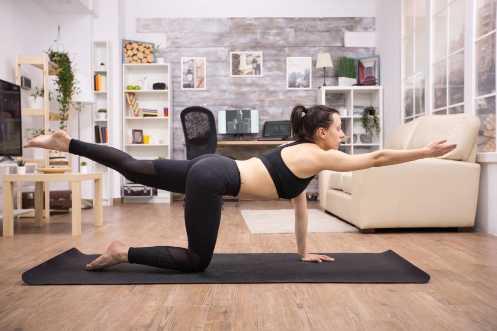 Young woman in legging doing balance yoga pose in living room.