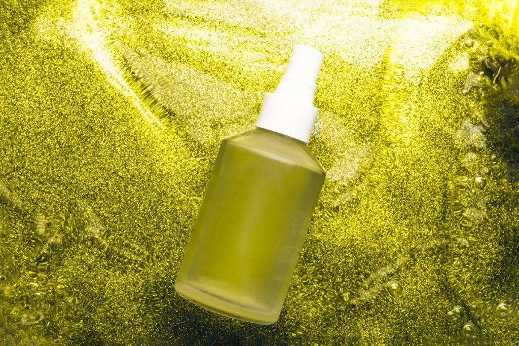 Mat glass bottle of body oil on yellow water background, glass cosmetics in water, top view