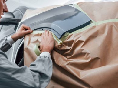 Covering car by brown cloth. Caucasian automobile repairman in uniform works in garage.